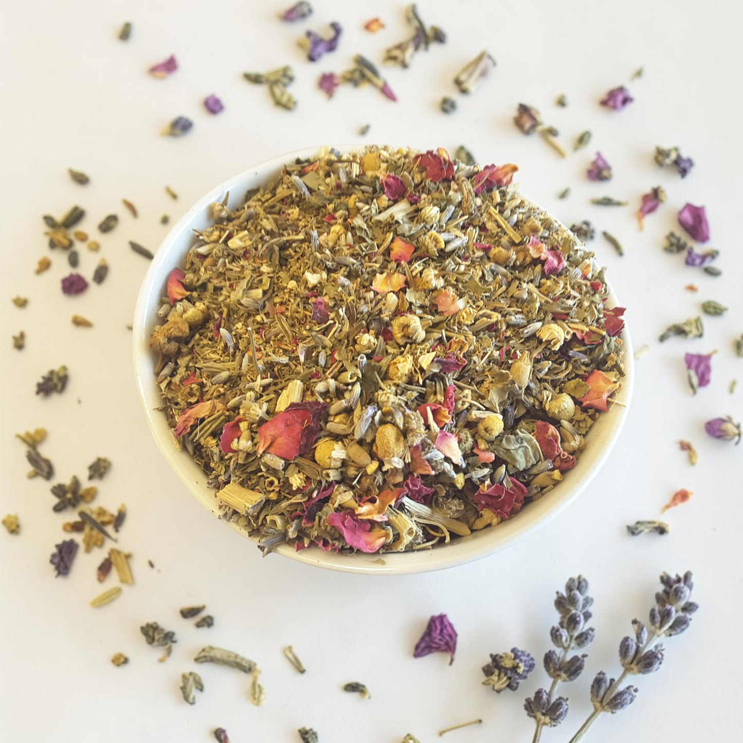 Intuition herbal tea mix in a white bowl with scattered herbs on a light background