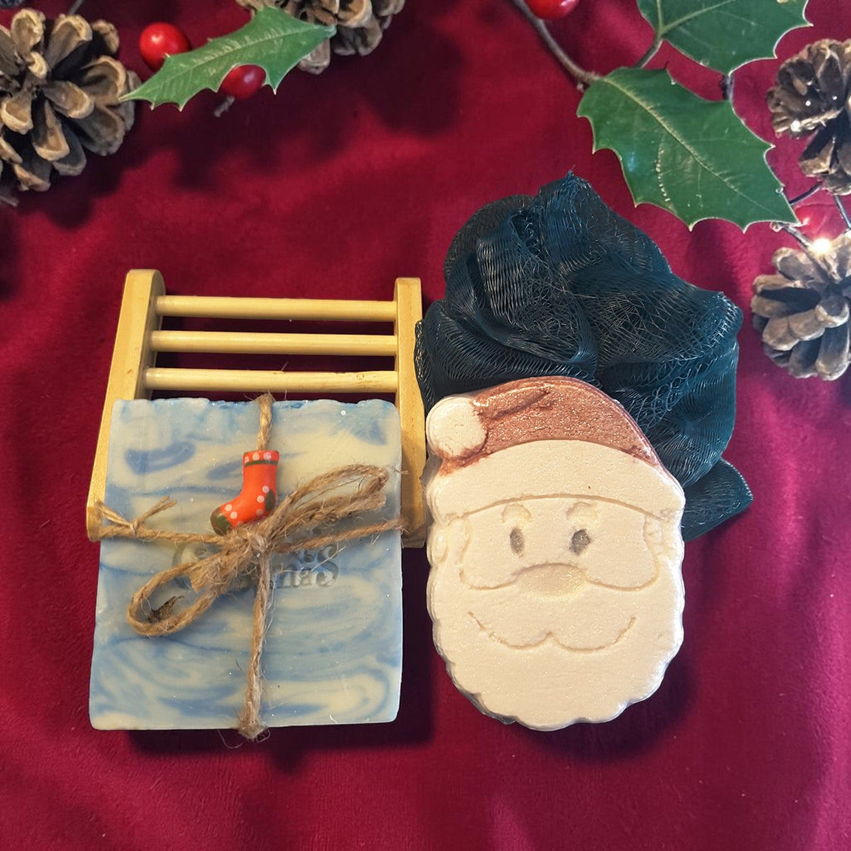 snowdrift christmas gift crate spa set featuring snowdrift soap, santa shaped bath bomb, bamboo soap ladder and loofah on a red fabric surface