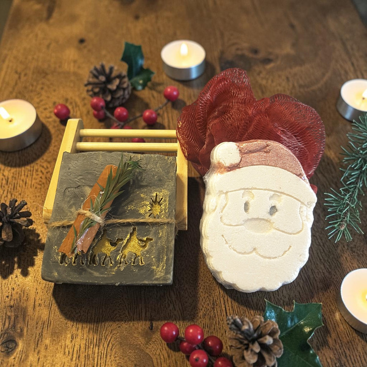 winter solstice christmas gift crate spa set featuring winter solstice soap, santa shaped bath bomb, bamboo soap ladder and loofah on a dark wooden surface with pinecones and tea light candles