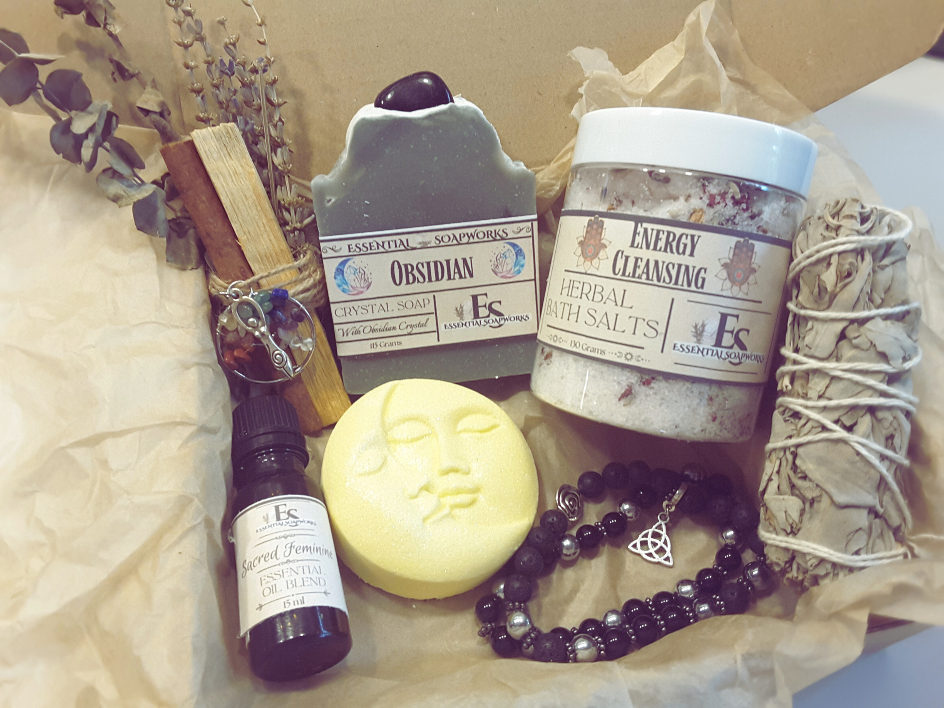 obsidian mind, body and spirit self-care kit with obsidian topped soap, bath salts, sun and moon bath bomb, sacred feminine essential oil blend, white sage smudge stick, palo santo, cinnamon, eucalyptus and lavender smoke cleansing stick, two obsidian crystal bracelets