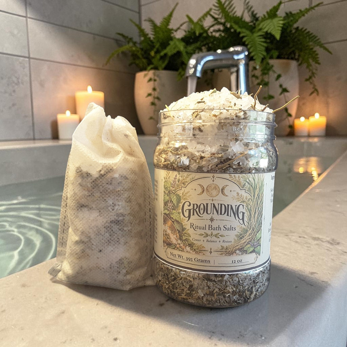 grounding bath salts in a jar alongside a muslin bag filled with bath salts on the edge of a bathtub with candles and greenery in the background