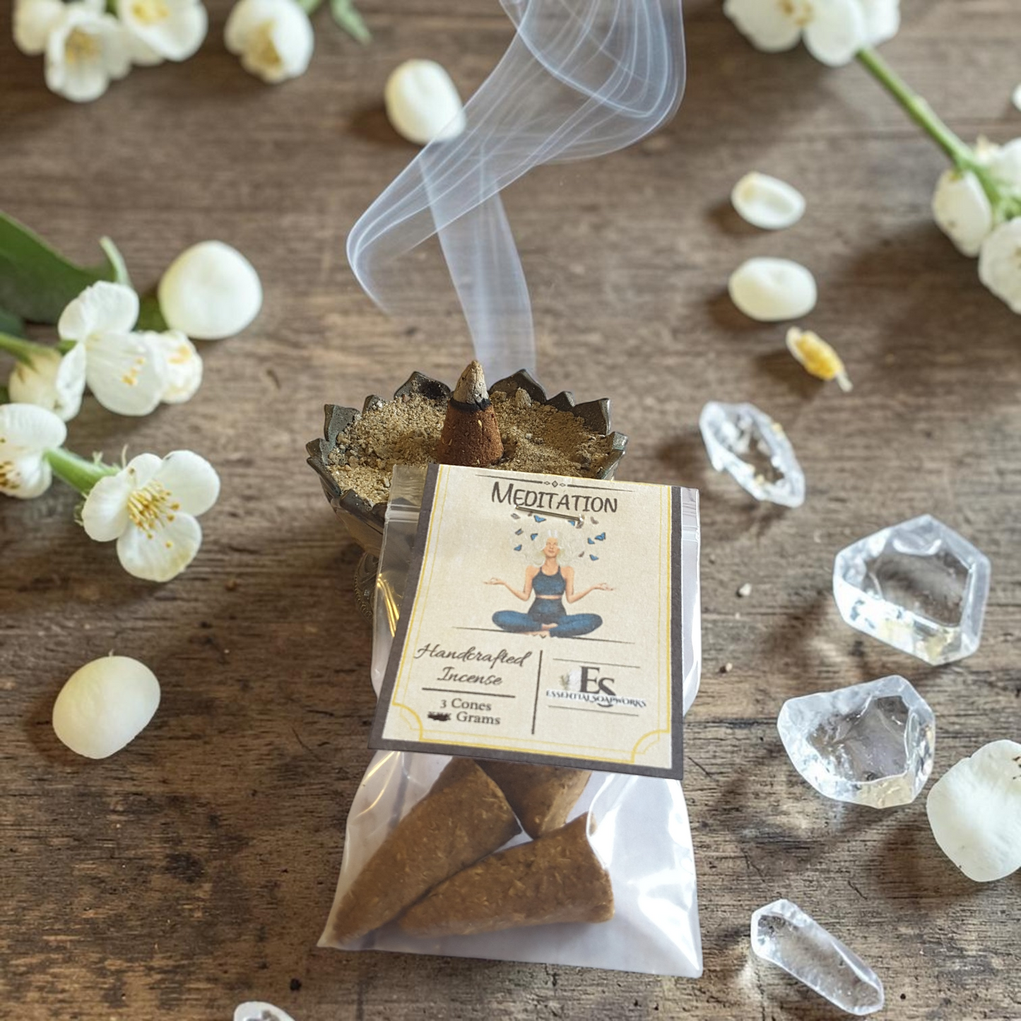 Meditation incense cones with smoke on a wooden surface with flowers and crystals.
