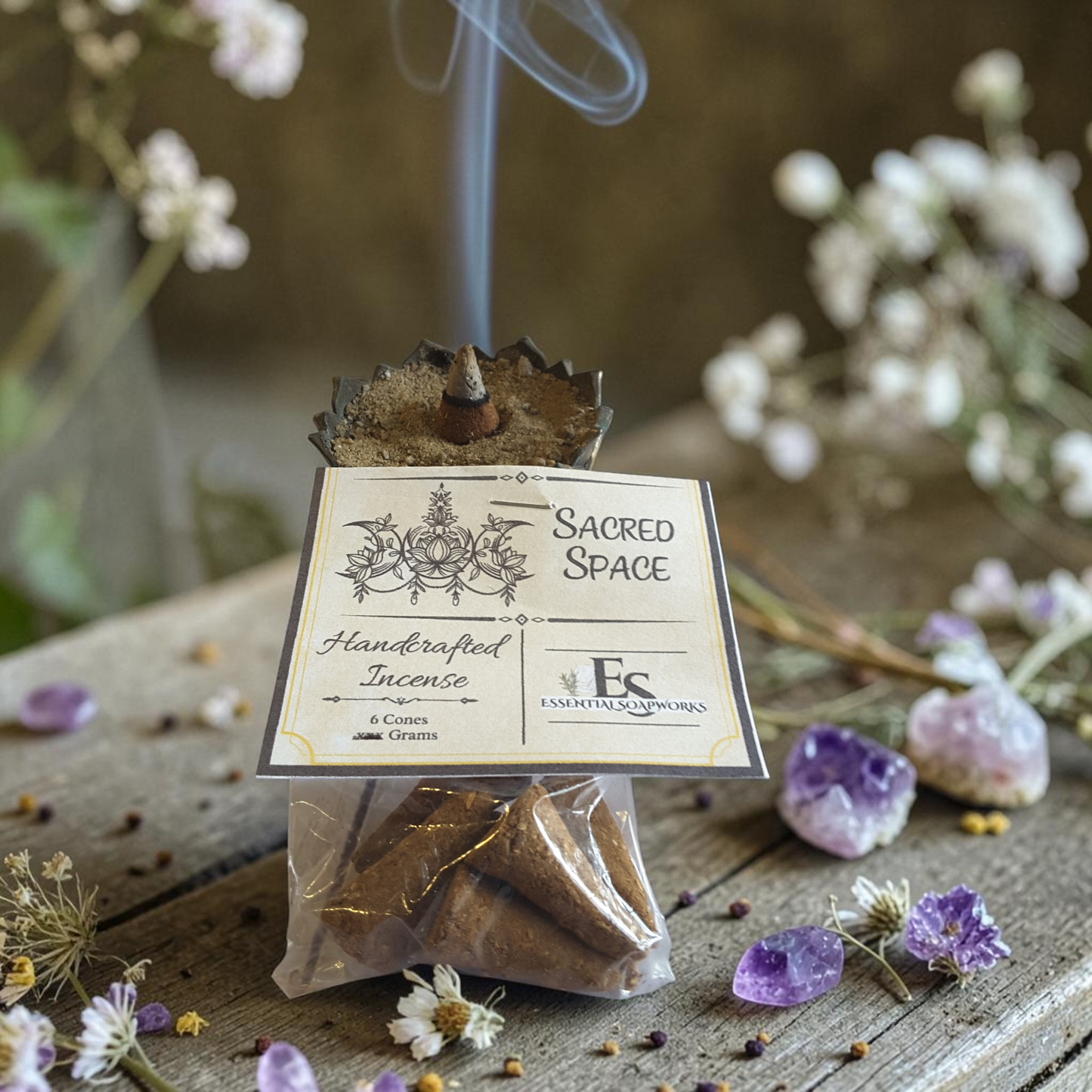 Handcrafted incense packaging with 'Sacred Space' label on a wooden surface with flowers and crystals.