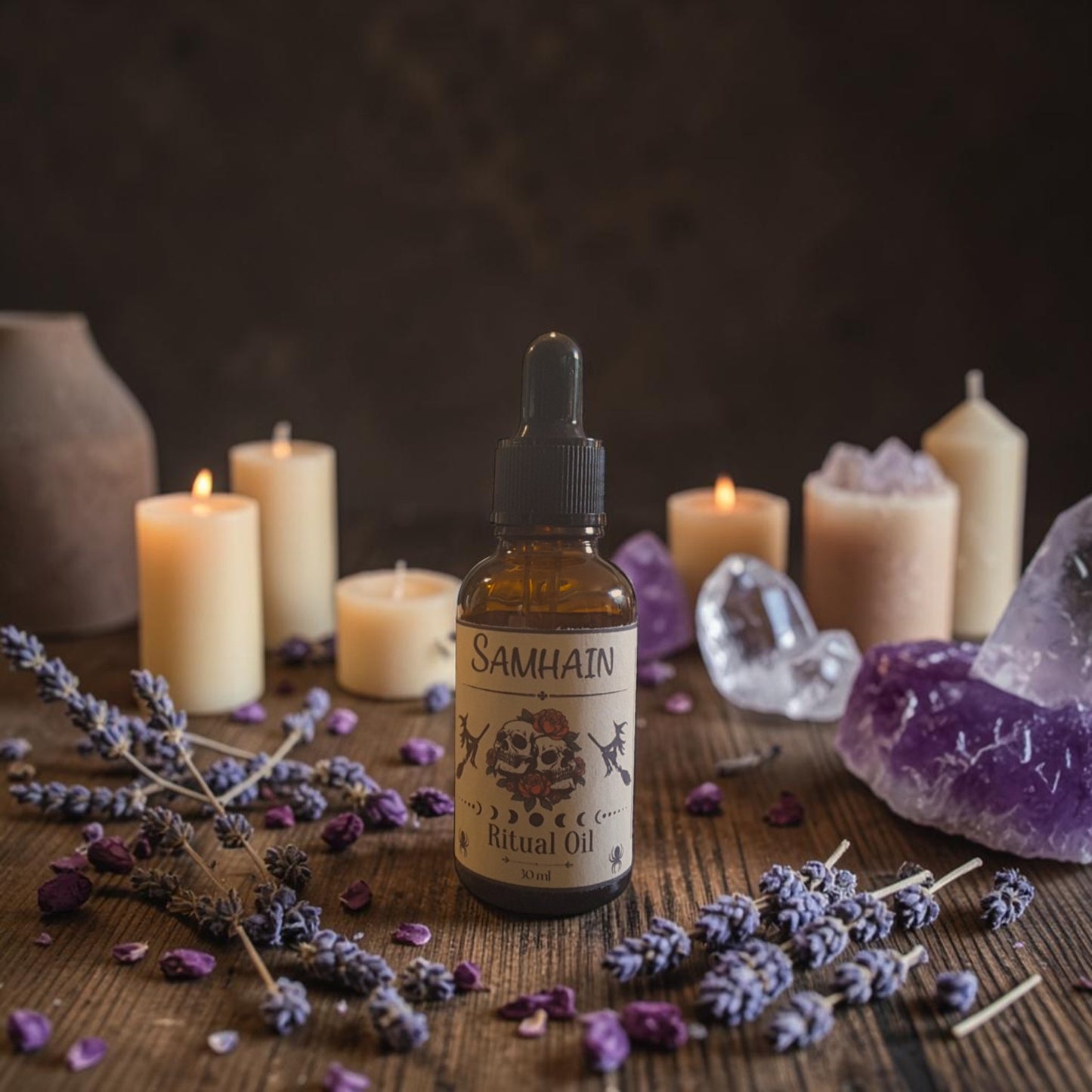 A bottle of Samhain Ritual Oil stands on a wooden surface surrounded by lit candles, lavender sprigs, dried petals, and purple crystal stones against a dark rustic background.