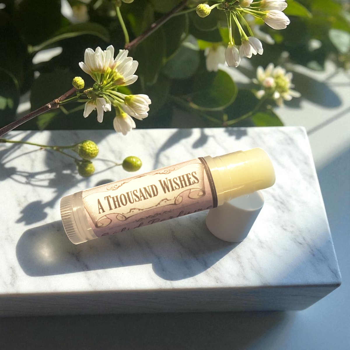 A Thousand Wishes solid perfume on a marble surface with flowers in the background