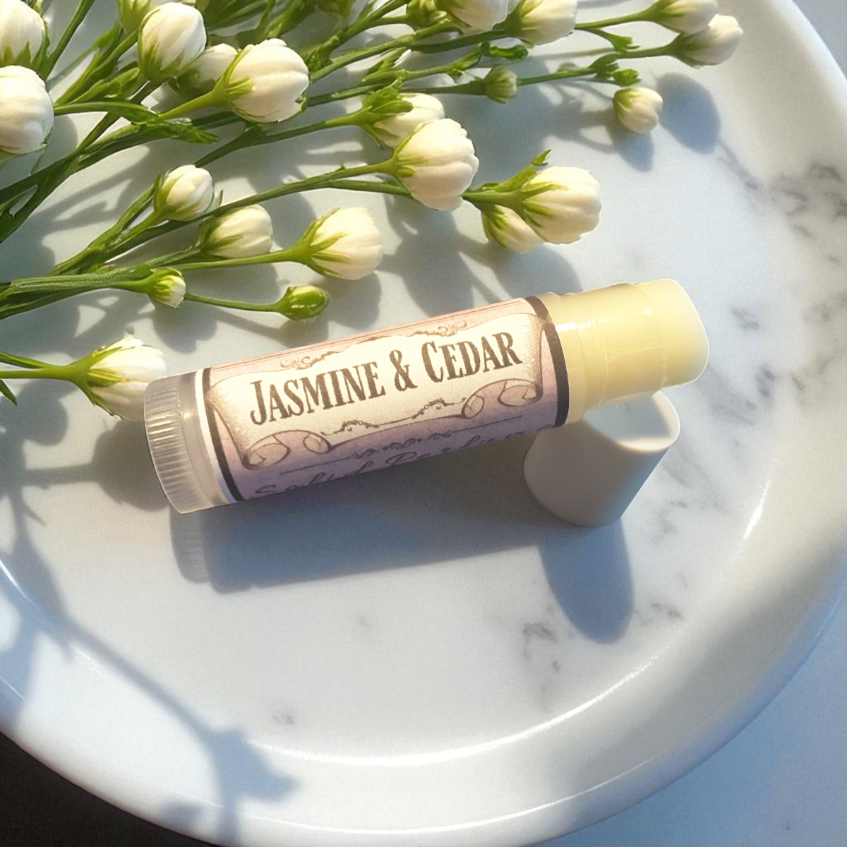 jasmine & Cedar solid perfume on a marble surface with white flowers.
