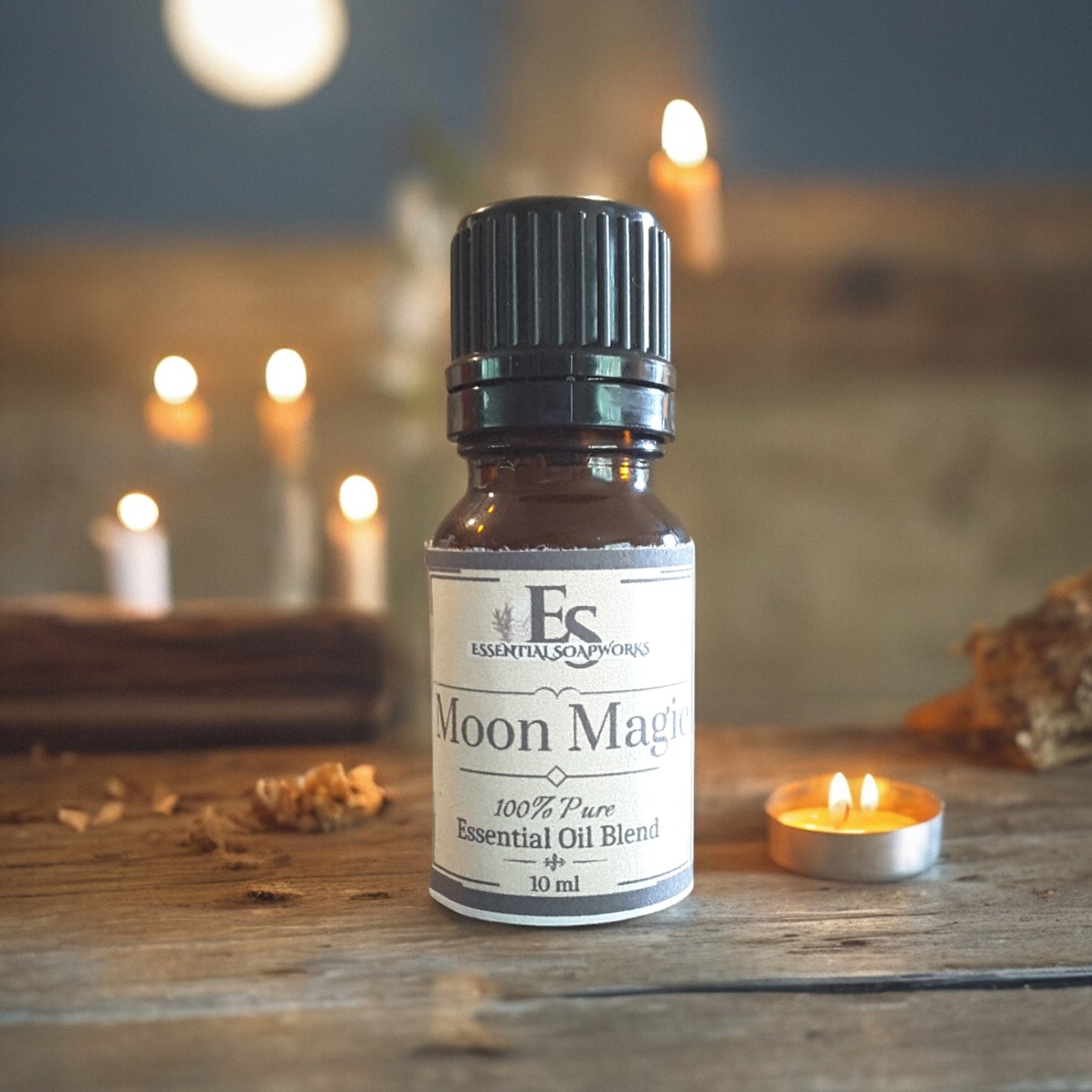 Bottle of Moon Magic essential oil diffuser blend on a wooden surface with candles in the background.