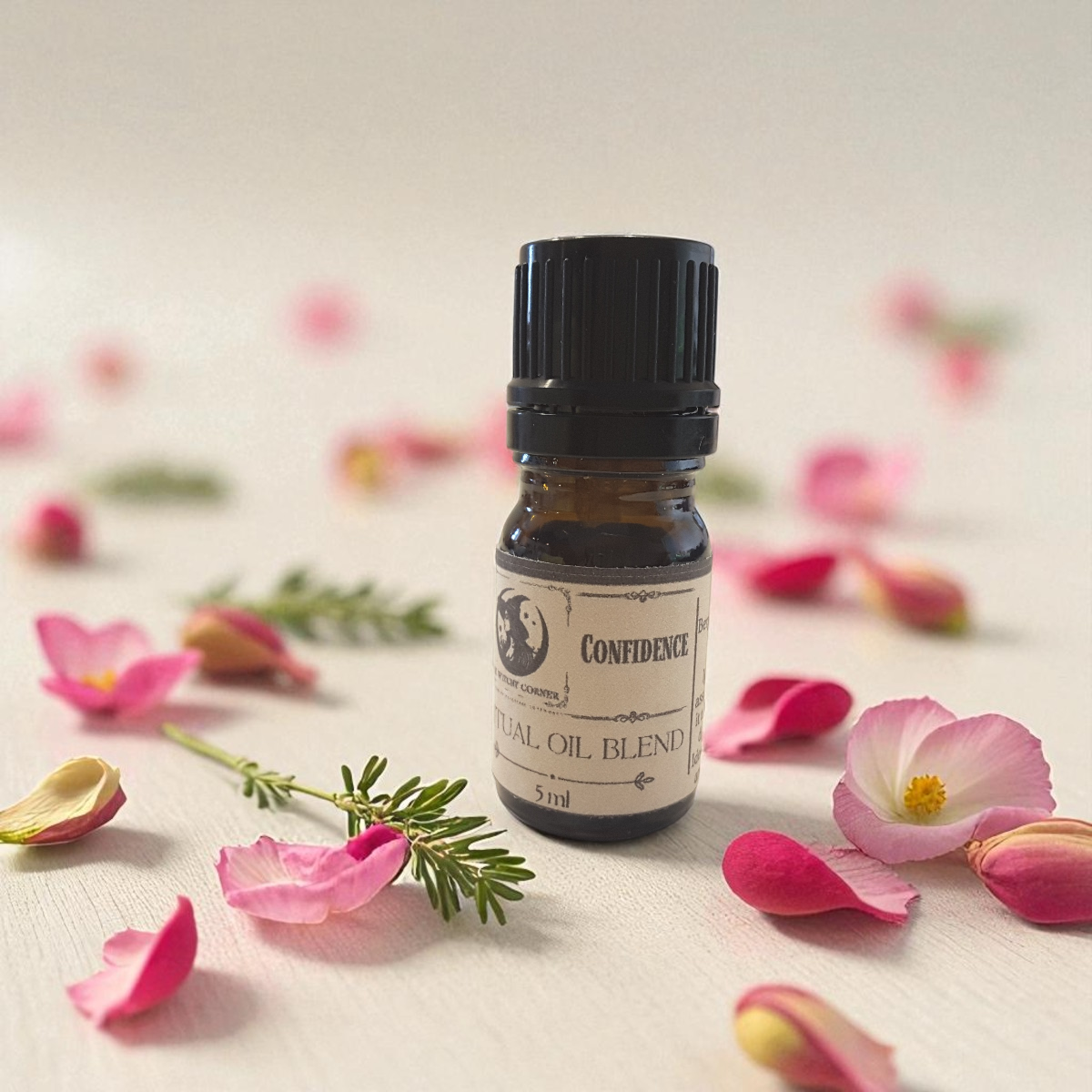 Small bottle of 'Confidence' essential oil blend surrounded by pink flowers on a light background
