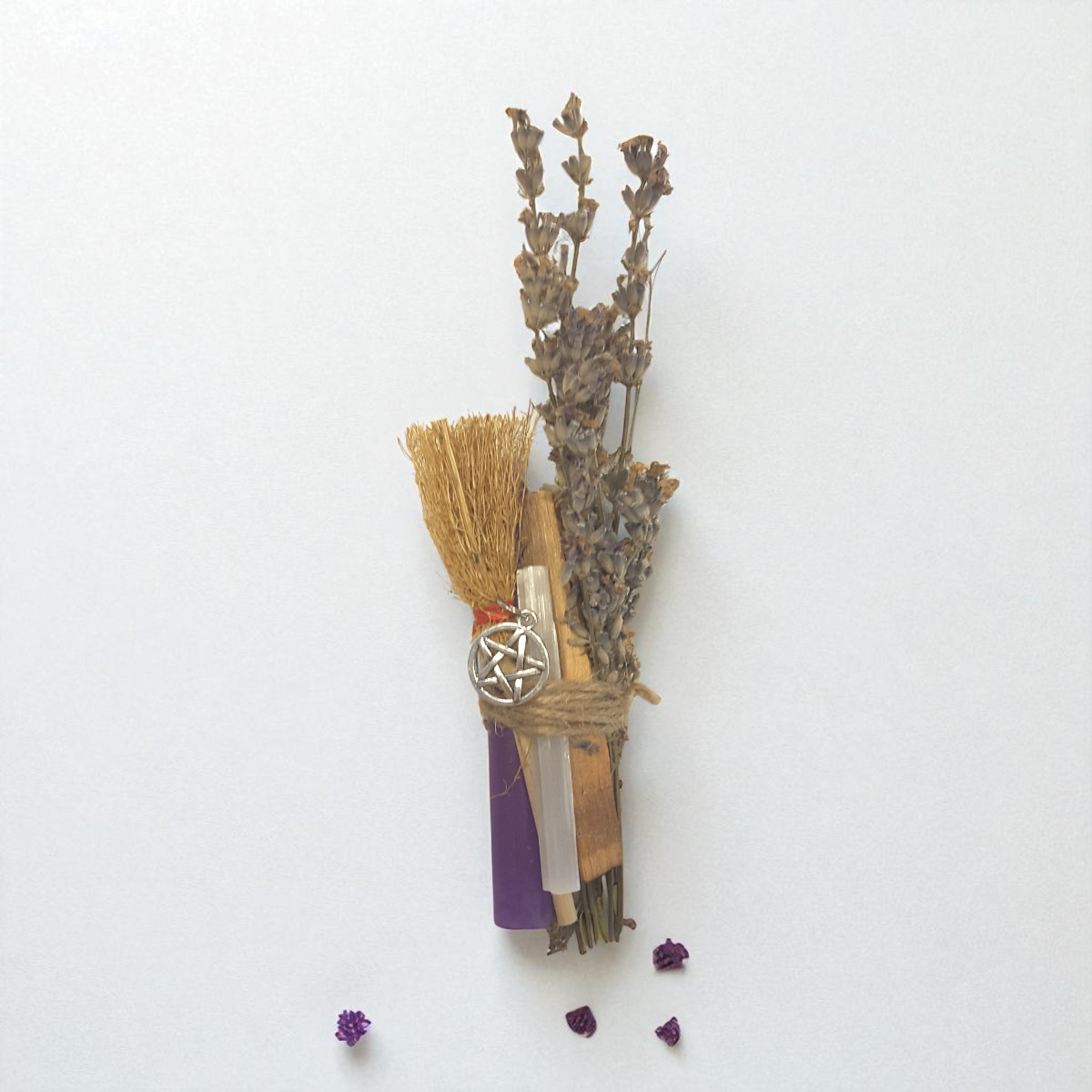 Bouquet of dried lavender, purple chime candle, sandalwood stick, selenite and mini besom tied with twine on a white background