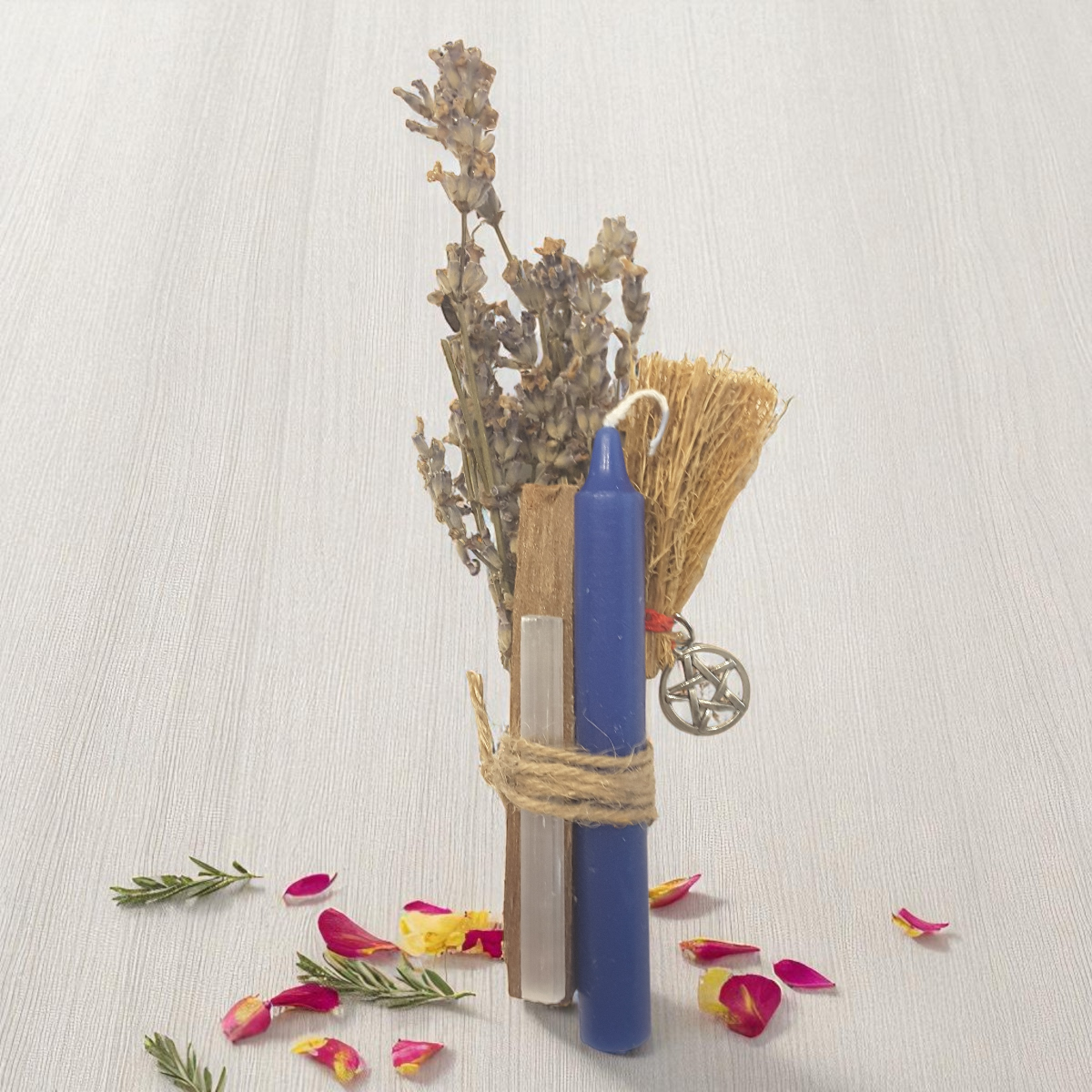 Blue candle, broom, and herbs on a light surface with scattered flowers.