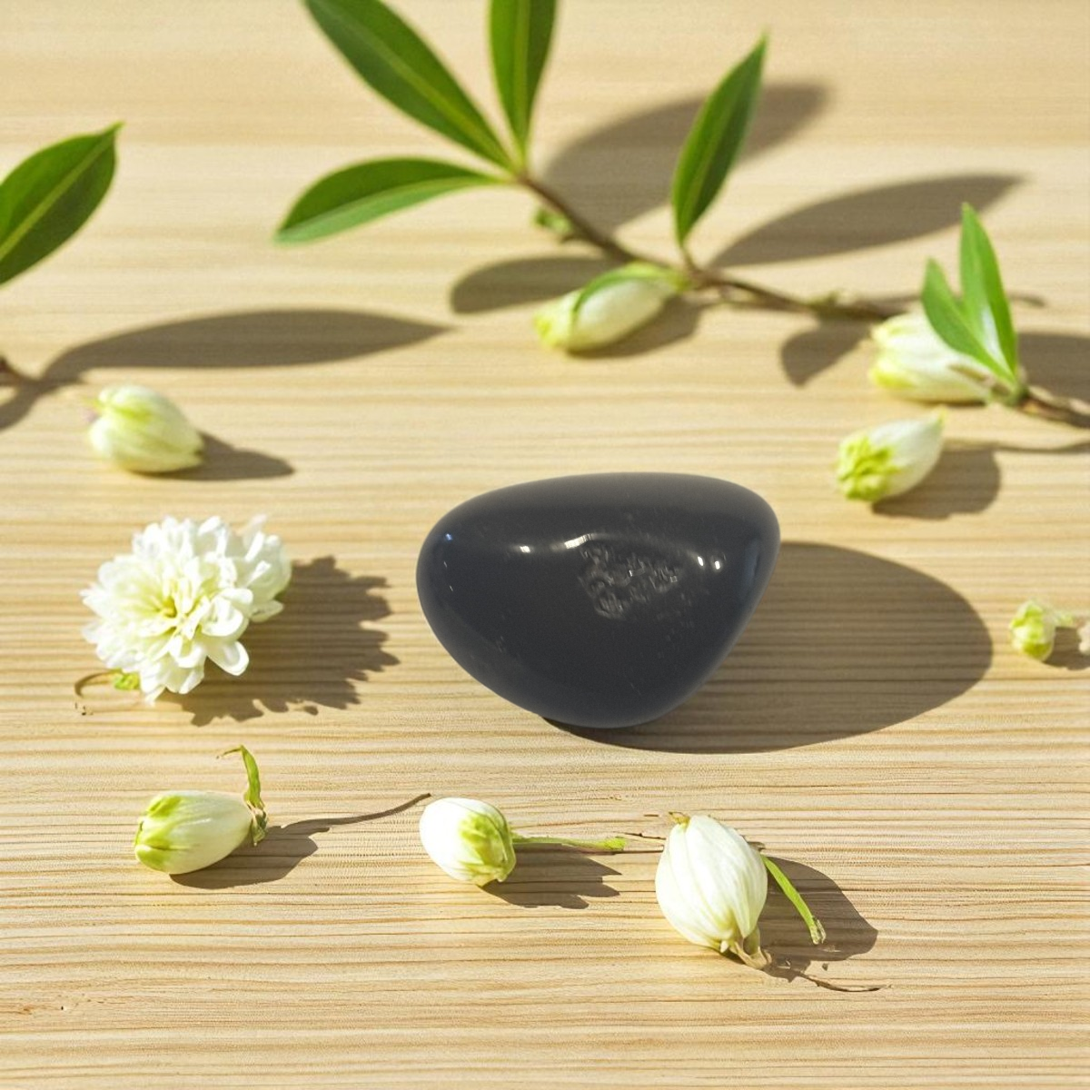 Obsidian crystal on a wooden surface with white flowers and green leaves
