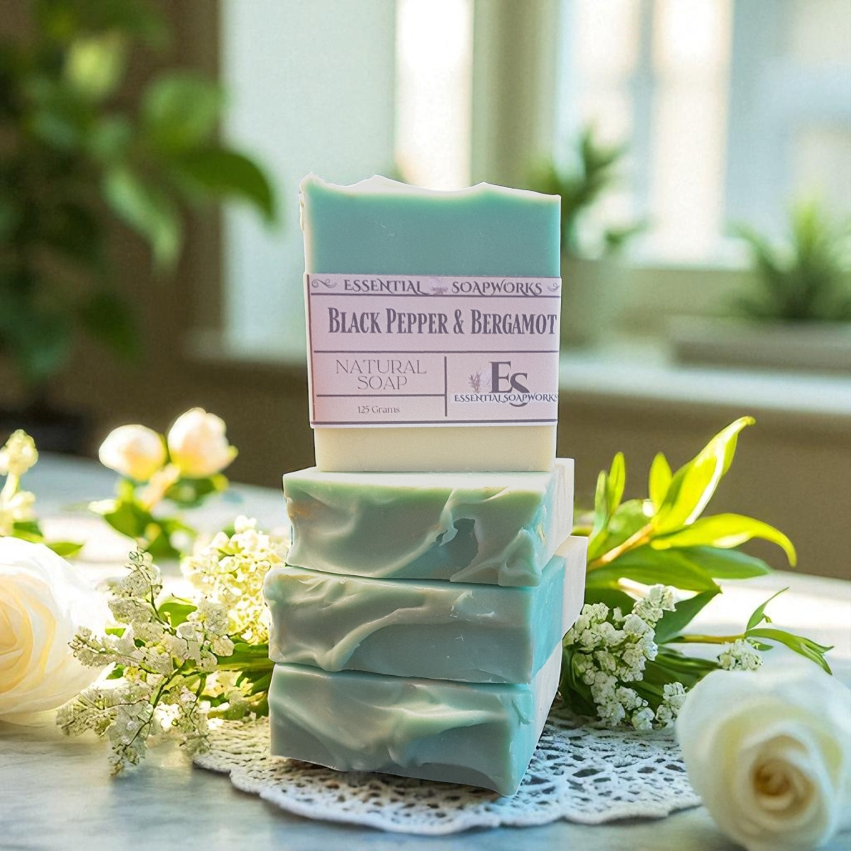 Stack of black pepper & bergamot natural soap bars with a visible brand label on a decorative mat with flowers.