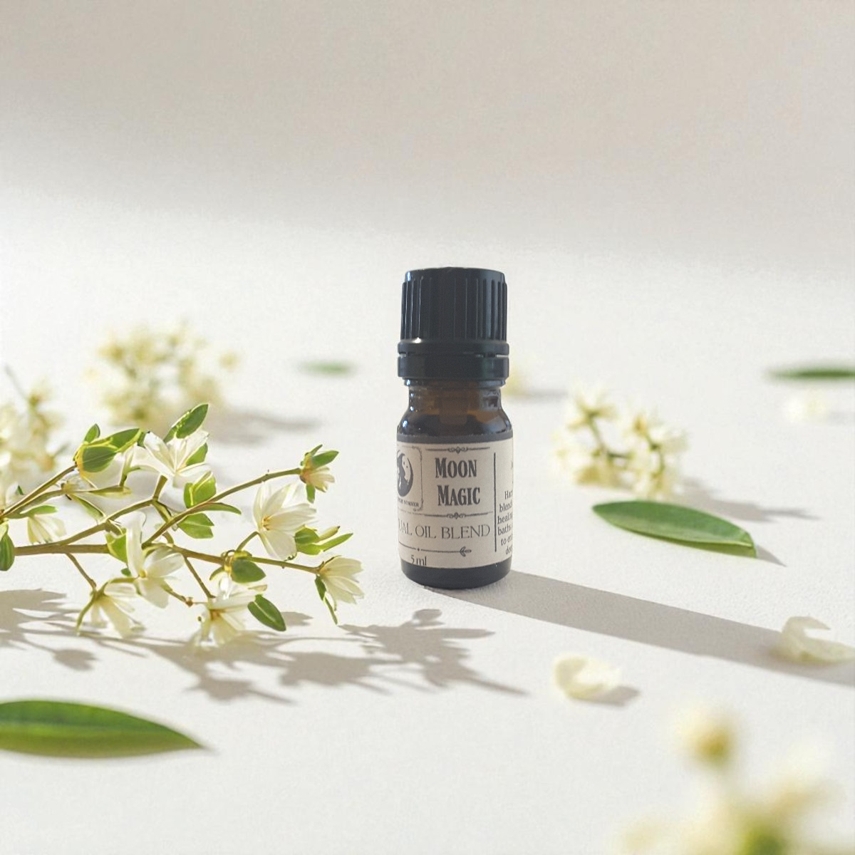 Moon Magic ritual oil blend surrounded by white flowers and green leaves on a light background