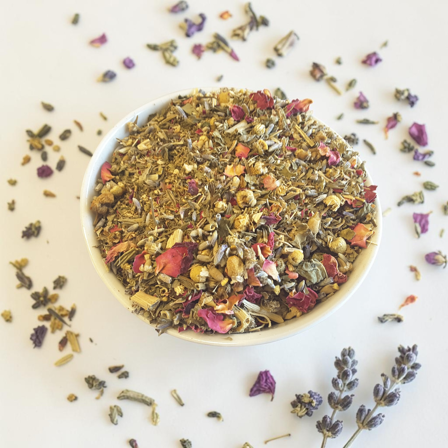 Intuition herbal tea mix in a white bowl with scattered herbs on a light background
