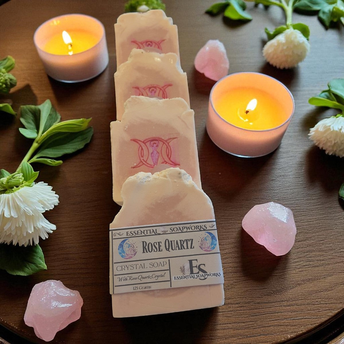 Rose Quartz crystal soap with candles and flowers on a wooden surface