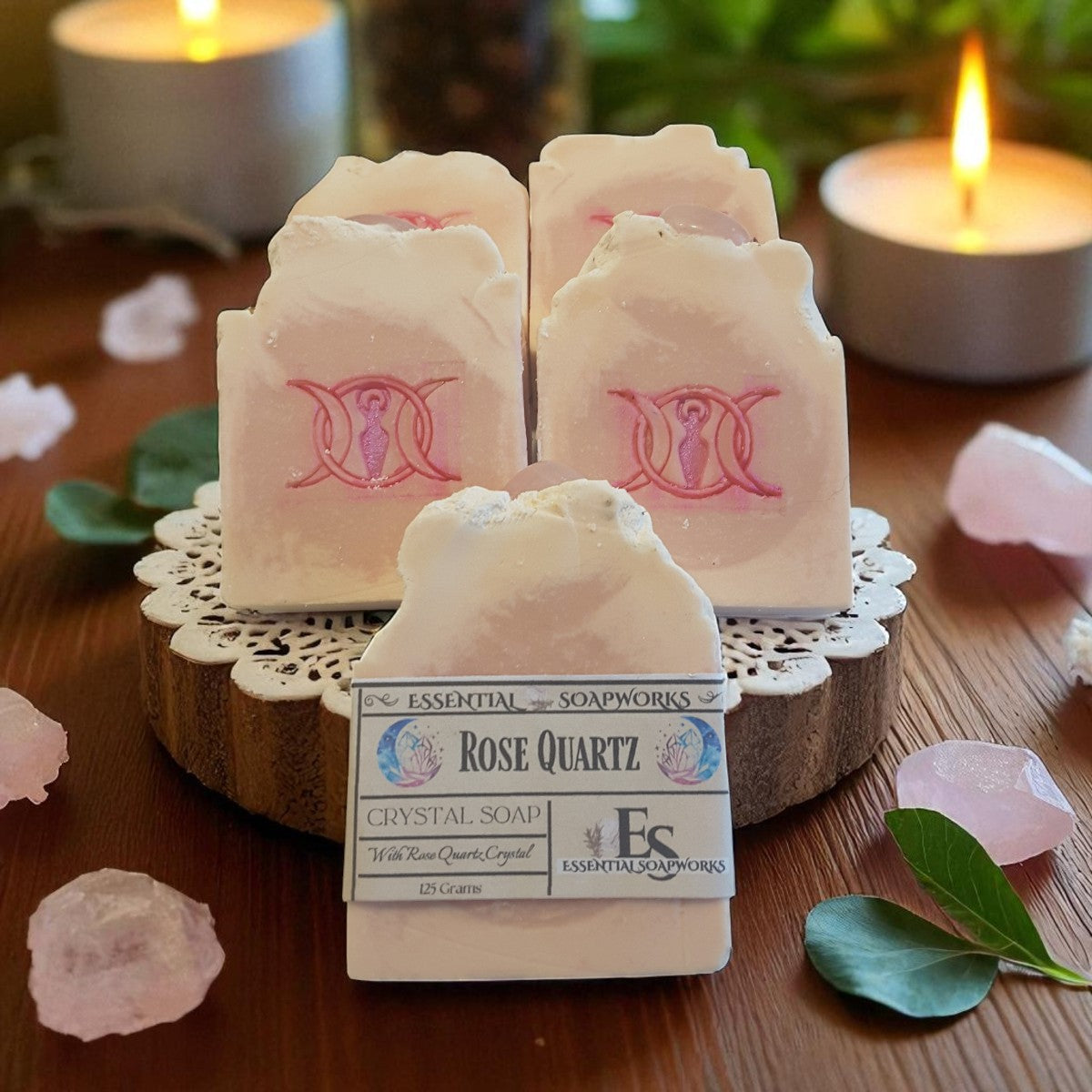 Rose Quartz crystal soap with a triple goddess symbol on a wooden surface with candles and flowers.