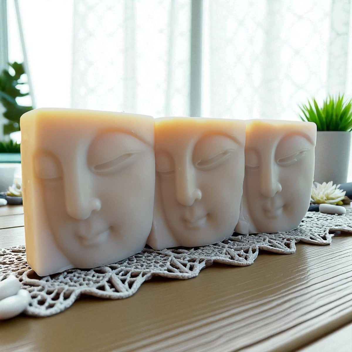 Three soap bars with a buddha face designs on a lace doily with a blurred indoor background