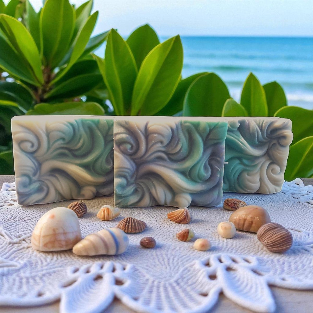 Three wave-patterned soap bars on a textured surface with shells and greenery in the background