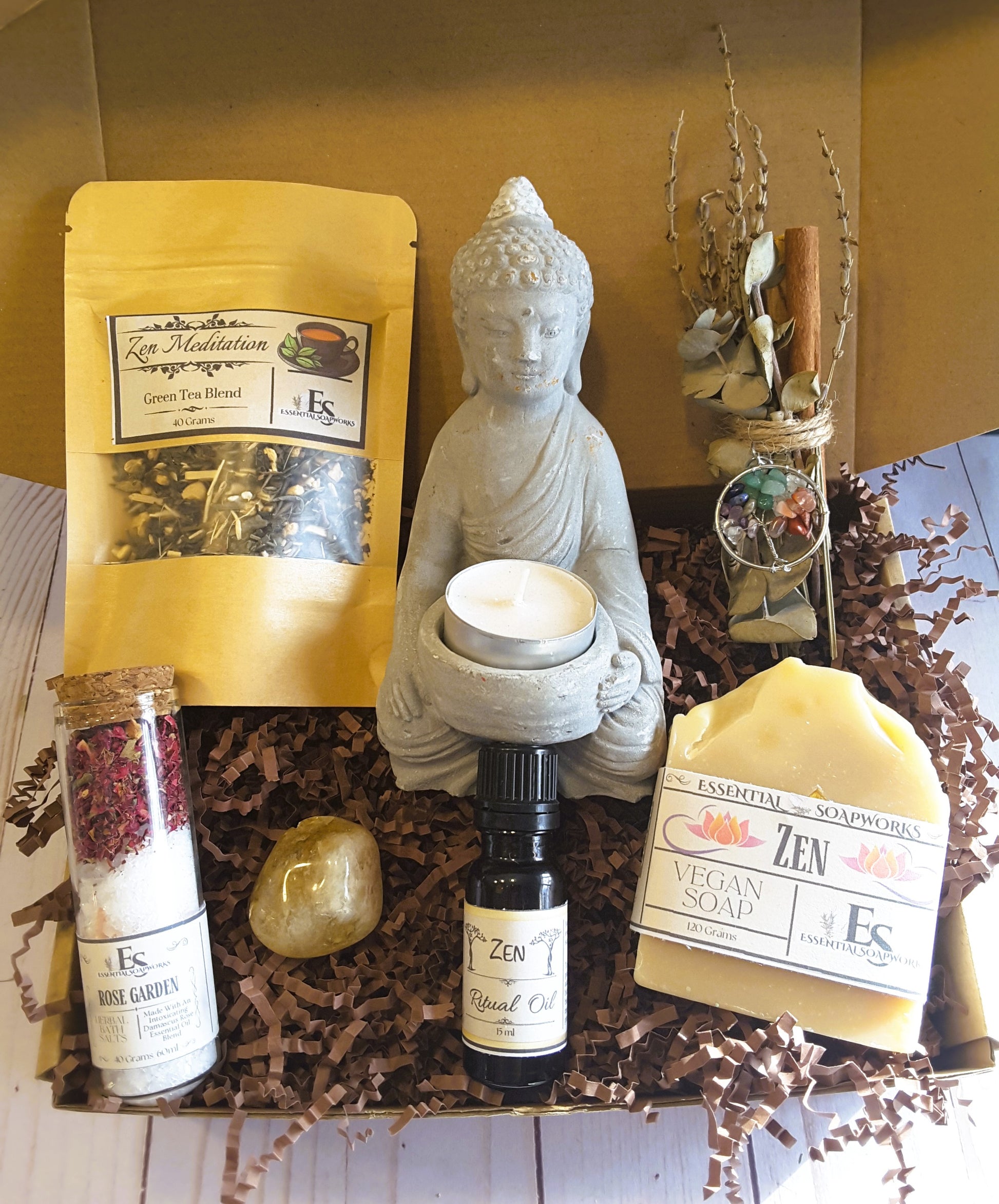 Collection of Zen-themed products including a Buddha statue candle holder, tea, soap, and ritual oil on a wooden surface.