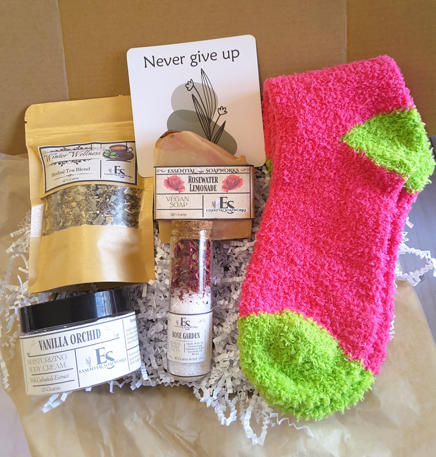 Holistic Self-Care Mystery Kit including pink and green socks, tea blend, soap, and other products on a textured surface.