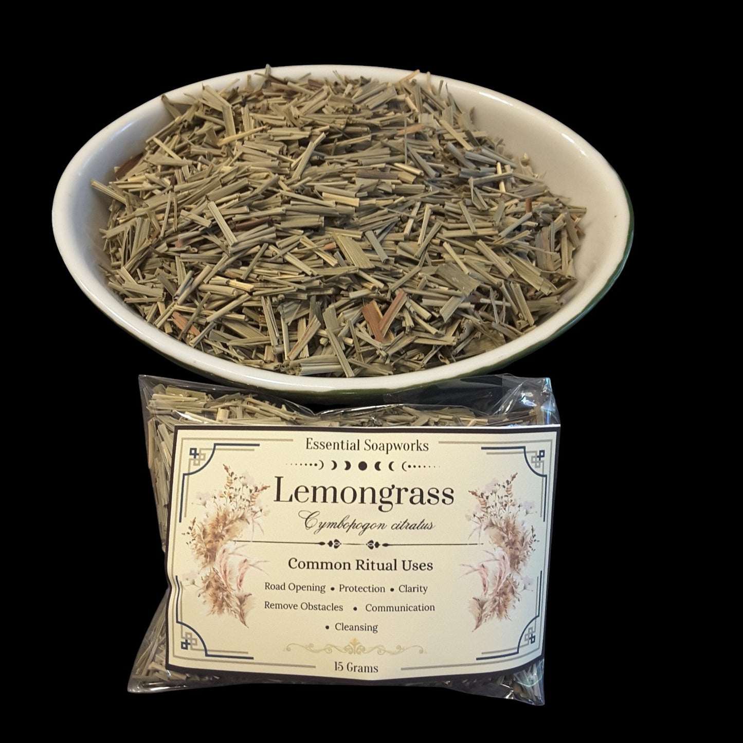 A bowl filled with dried lemongrass herb pieces above a clear plastic bag of the same herb with a printed label reading 'Lemongrass' and 'Essential Soapworks.' The background is solid black.