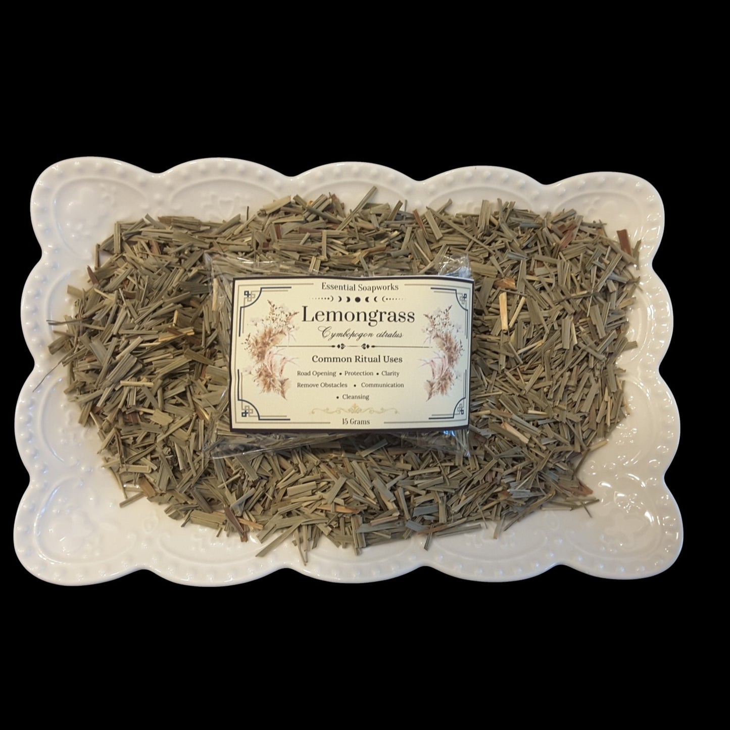 Dried lemongrass botanicals arranged on a white scalloped ceramic dish with a central product label reading 'Lemongrass' against a black background.