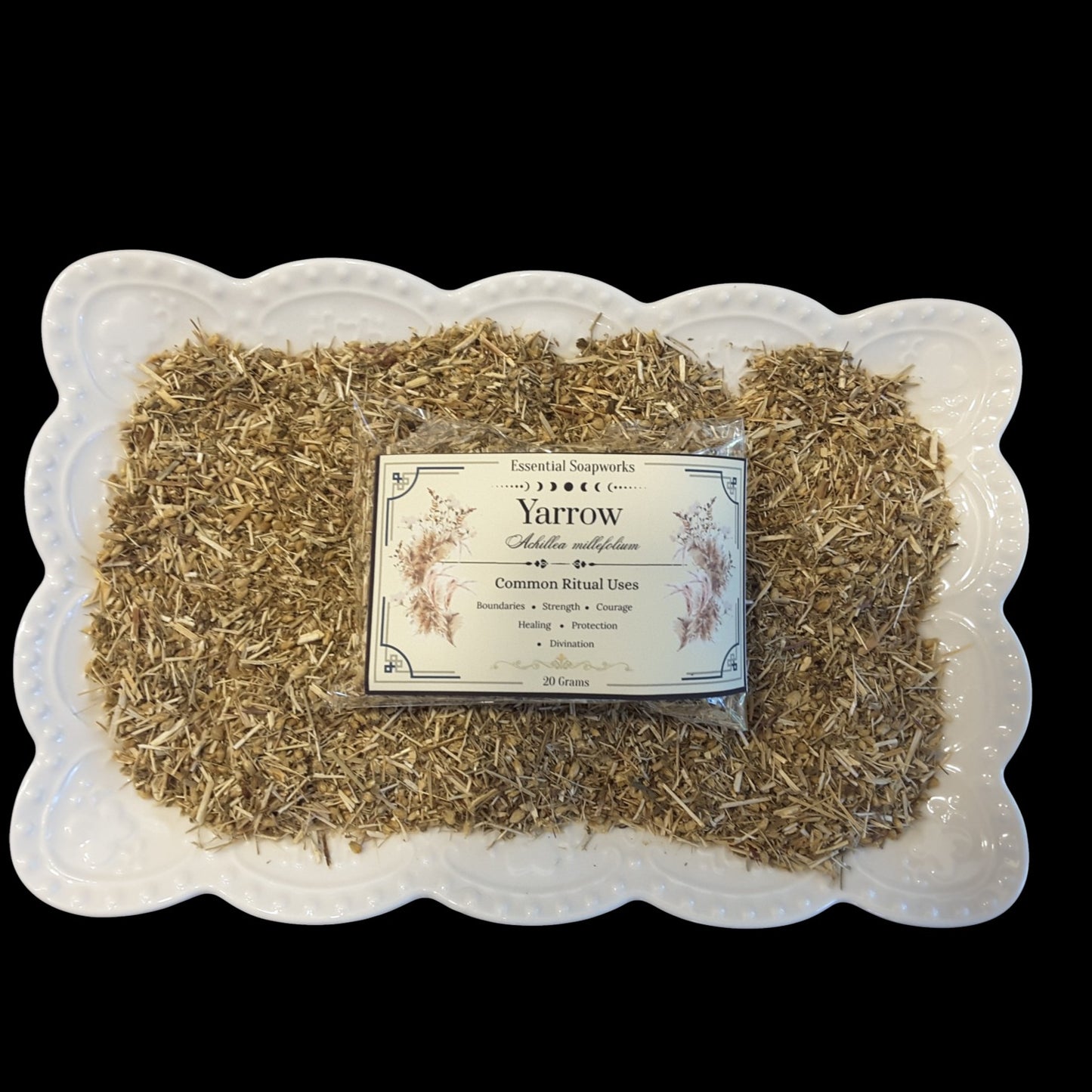 A white scalloped ceramic platter filled with yarrow herb, with a small packaged label reading 'Yarrow' placed in the center, against a solid black background.