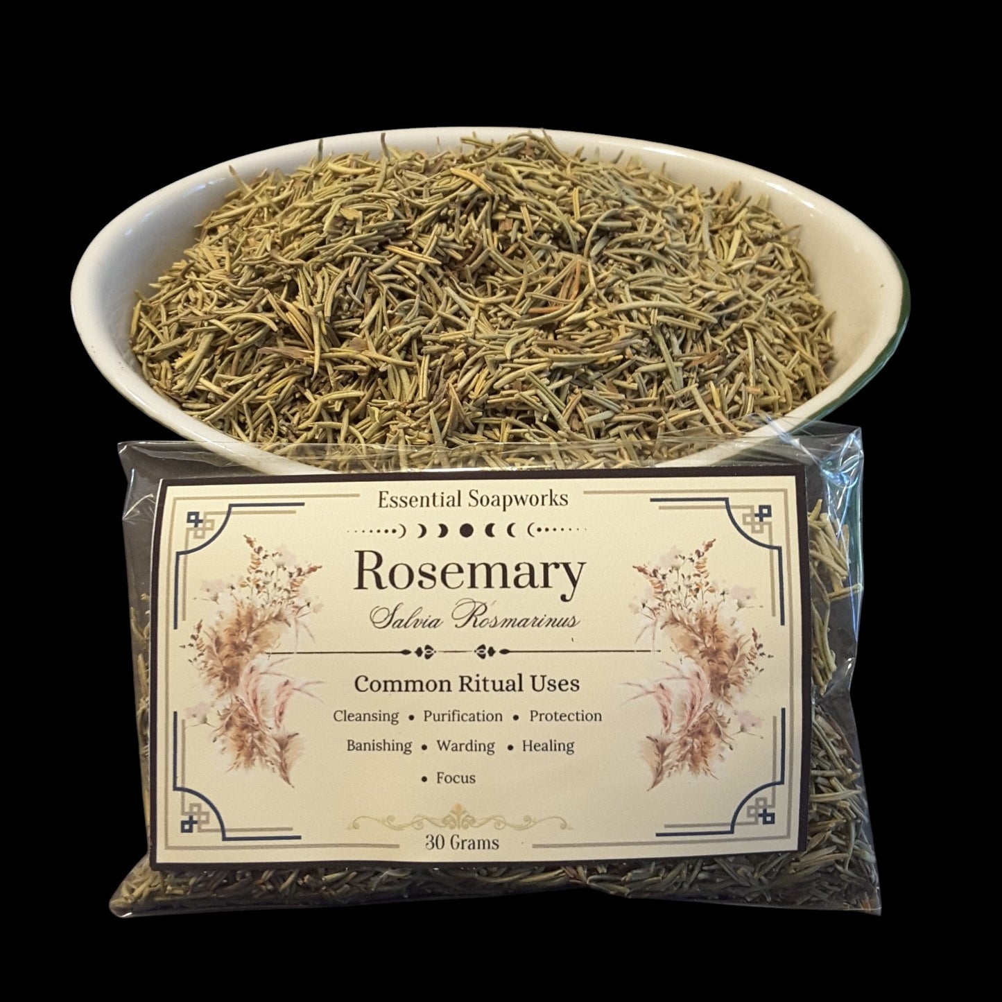 A clear plastic bag of rosemary with a cream label, shown in front of a white bowl filled with dried rosemary on a black background. 
