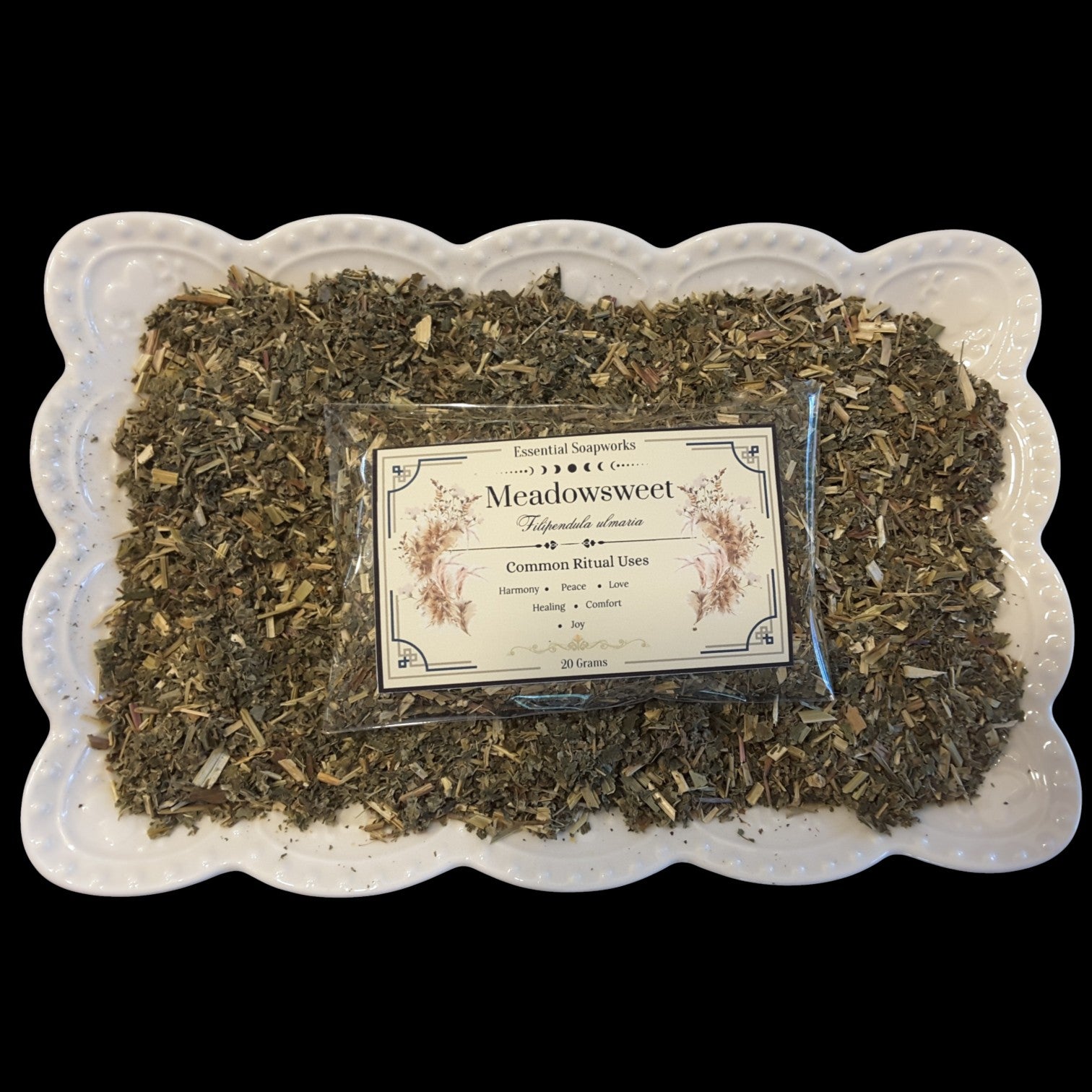A white scalloped ceramic dish filled with meadowsweet with a clear plastic packet labeled 'Meadowsweet' placed in the center on a black background.