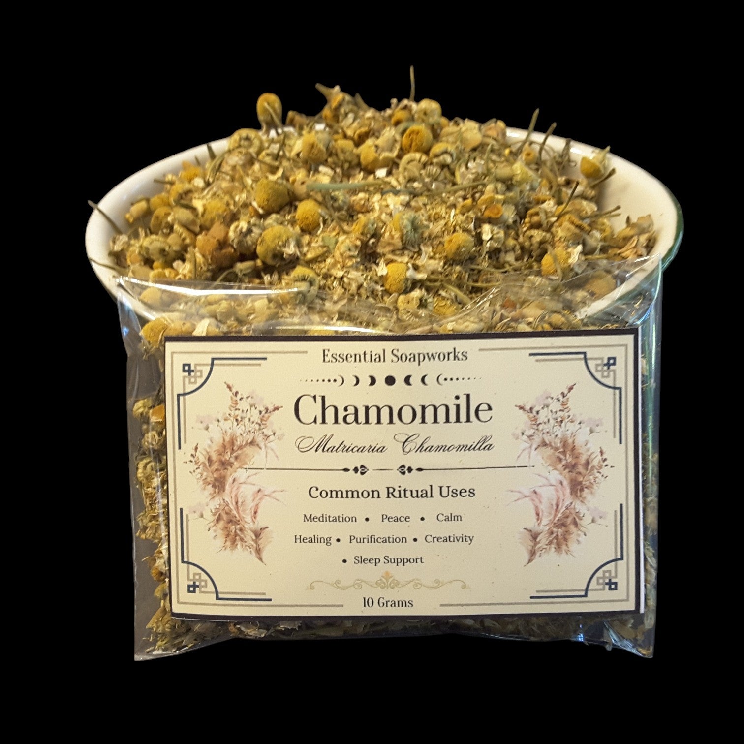 Chamomile flowers from Essential Soapworks in a clear plastic bag with a white label, filled with dried chamomile flowers on a black background.