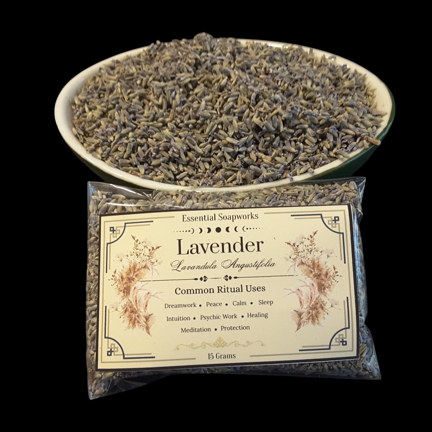 A clear plastic bag of lavender buds with a cream label reading 'Lavender' and 'Essential Soapworks,' placed in front of a white bowl filled with dried lavender buds on a black background.