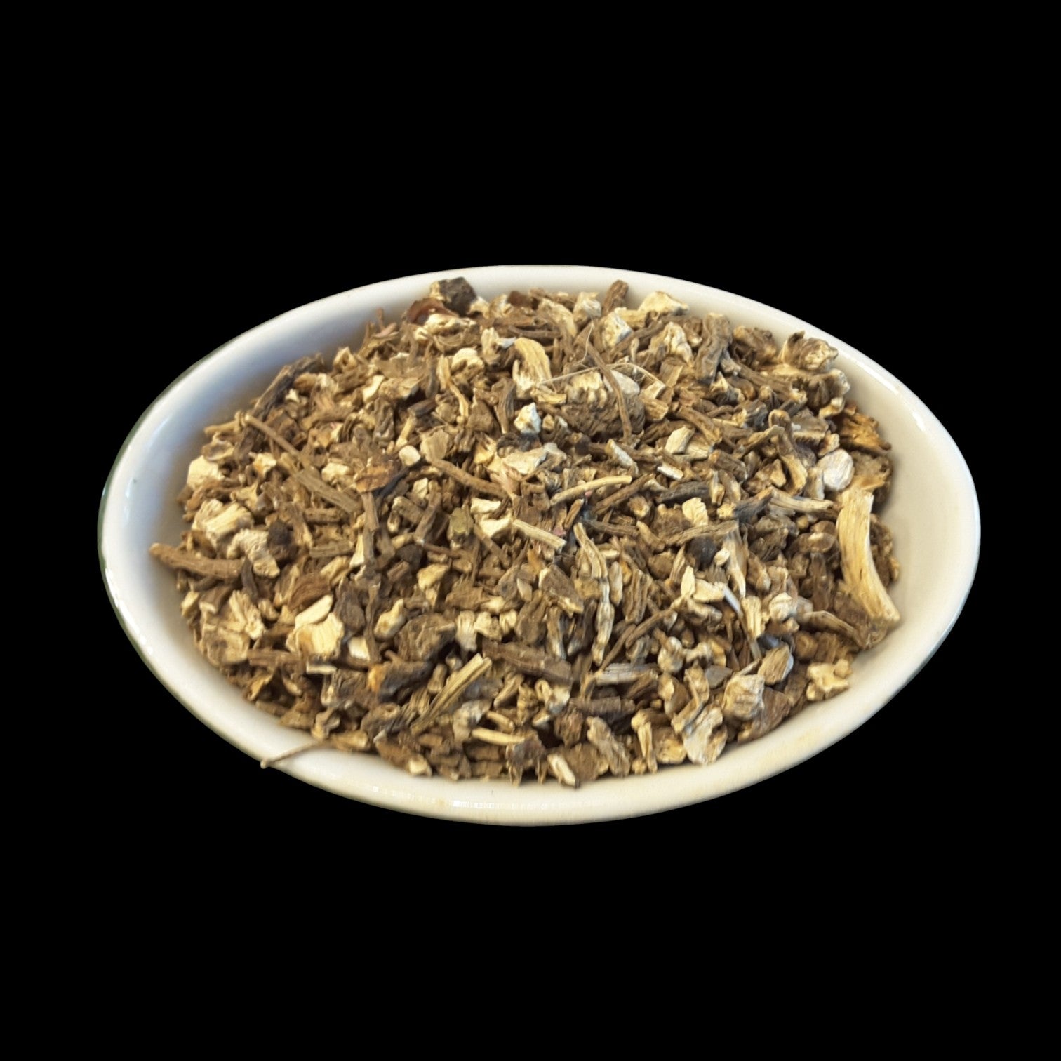 A white oval bowl filled with Angelica Root for witchcraft photographed against a solid black background.