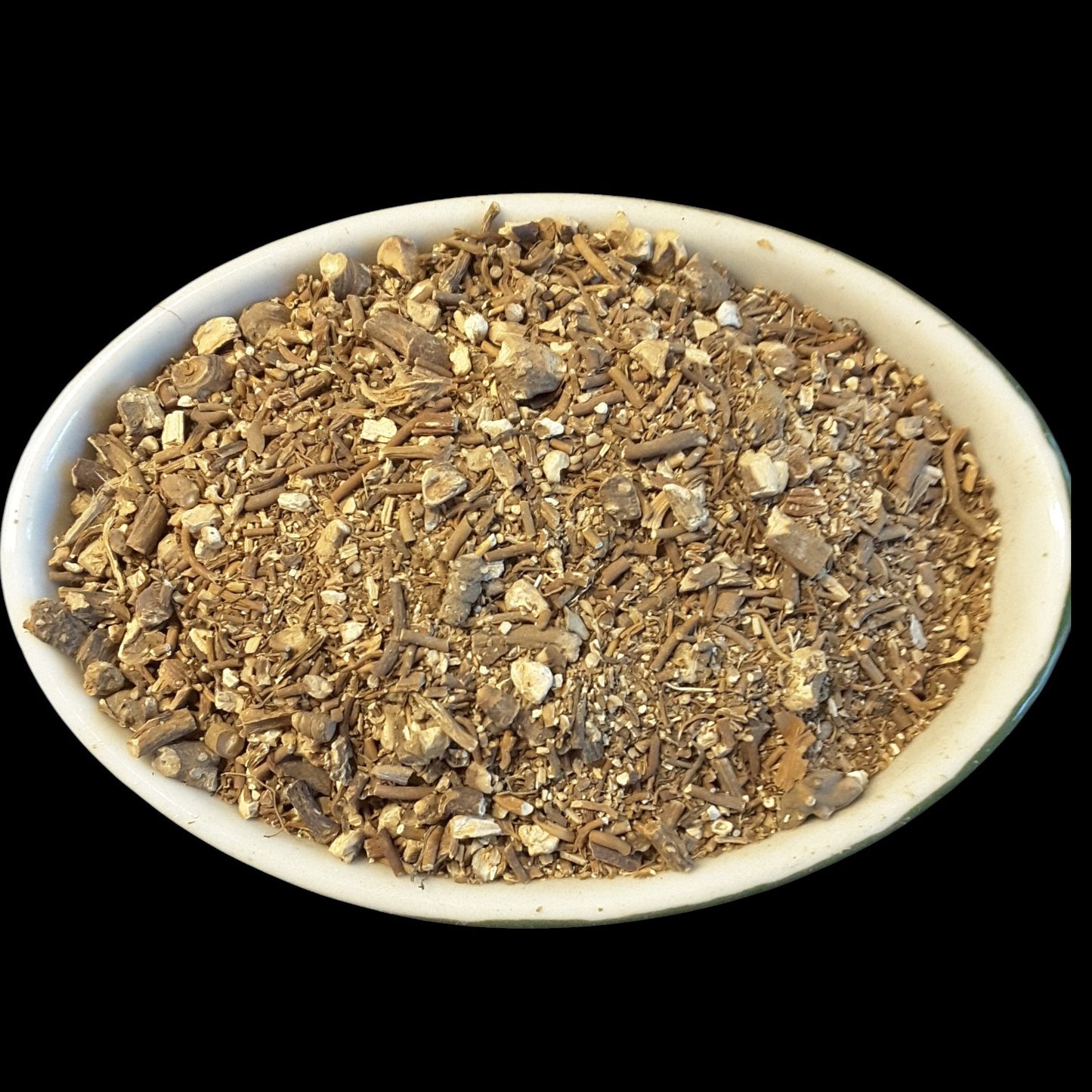 A white oval dish filled with mandrake root photographed against a solid black background.