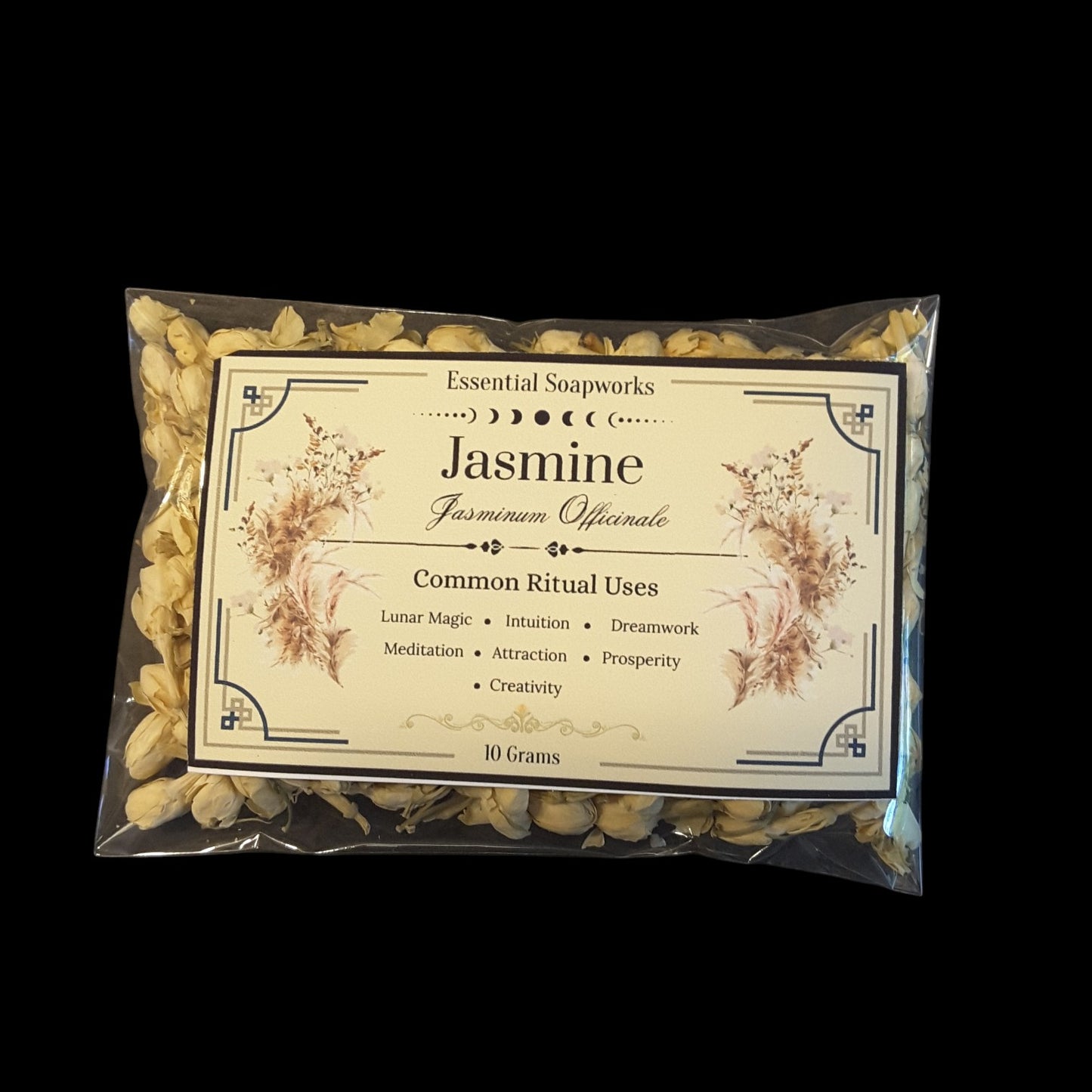 A clear plastic bag containing dried jasmine flowers with a large cream-colored paper label. The label reads 'Essential Soapworks Jasmine Jasminum Officinale' and lists common ritual uses, set against a solid black background.