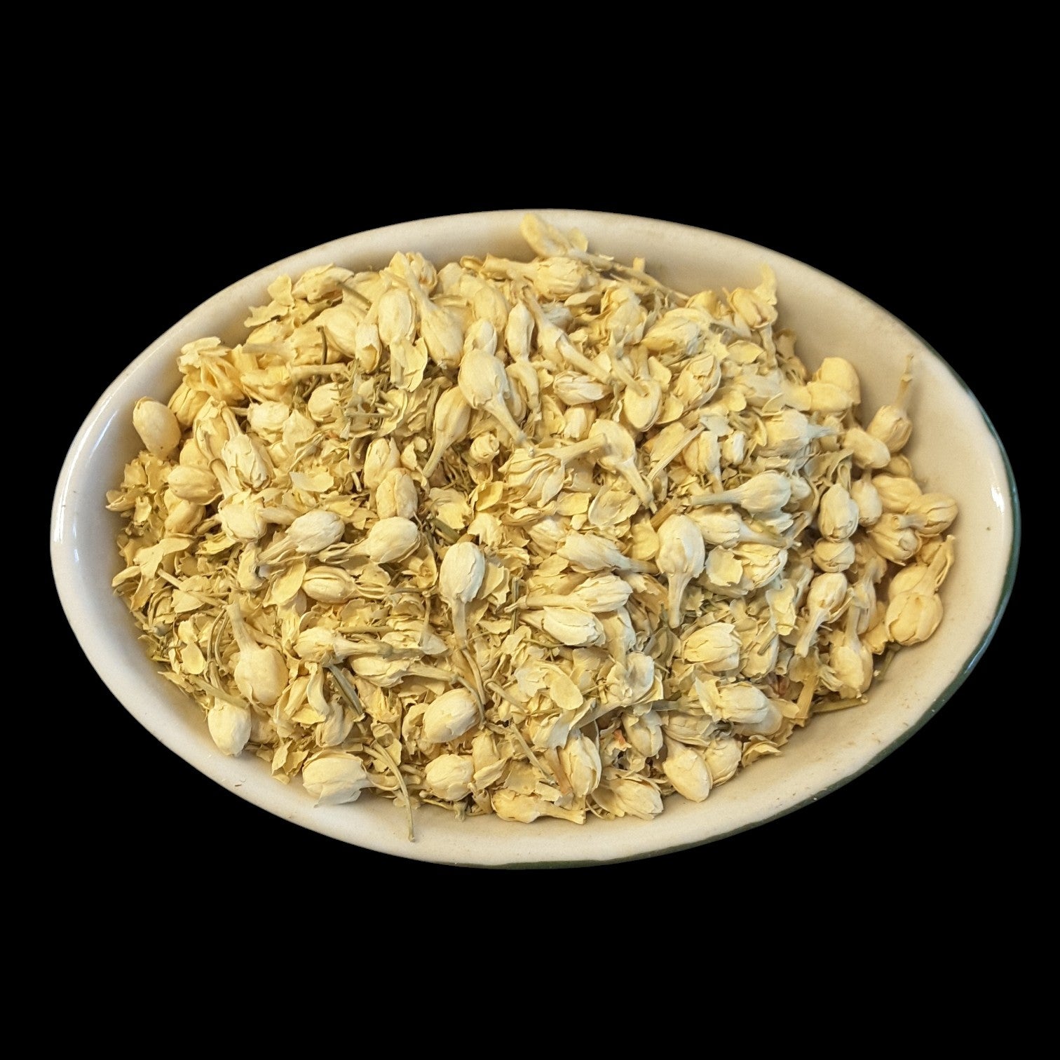A white oval bowl filled with dried white jasmine flowers, photographed against a solid black background.