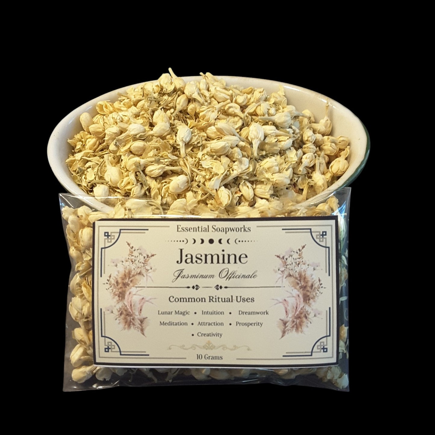 A clear plastic bag of Essential Soapworks Jasmine (Jasminum Officinale) 10 grams, with a white bowl filled with dried pale yellow jasmine buds placed behind it, set against a solid black background.