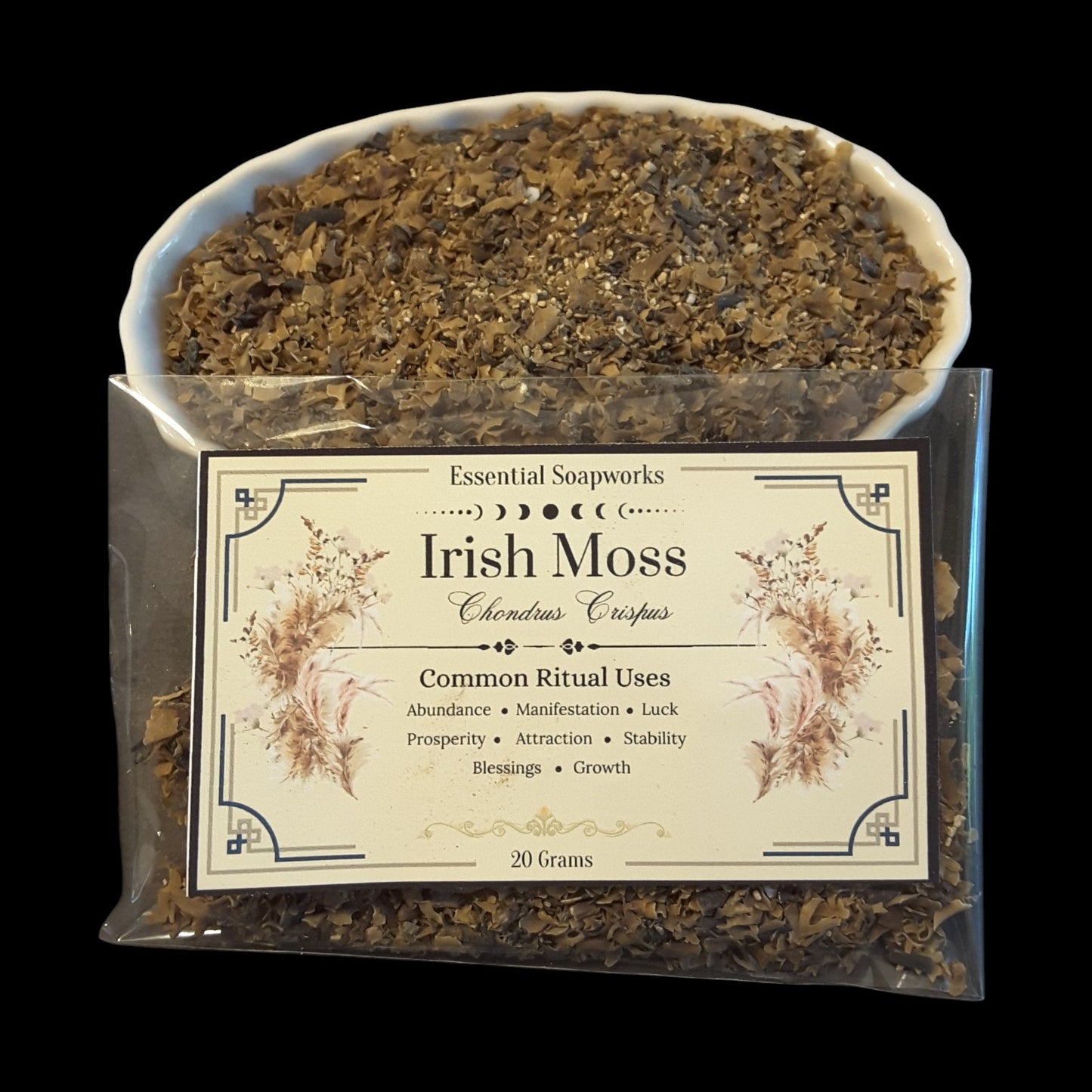 A clear plastic bag of Irish Moss Chondrus Crispus, with a white bowl filled with the dried brown seaweed pieces placed behind the package, on a black background.