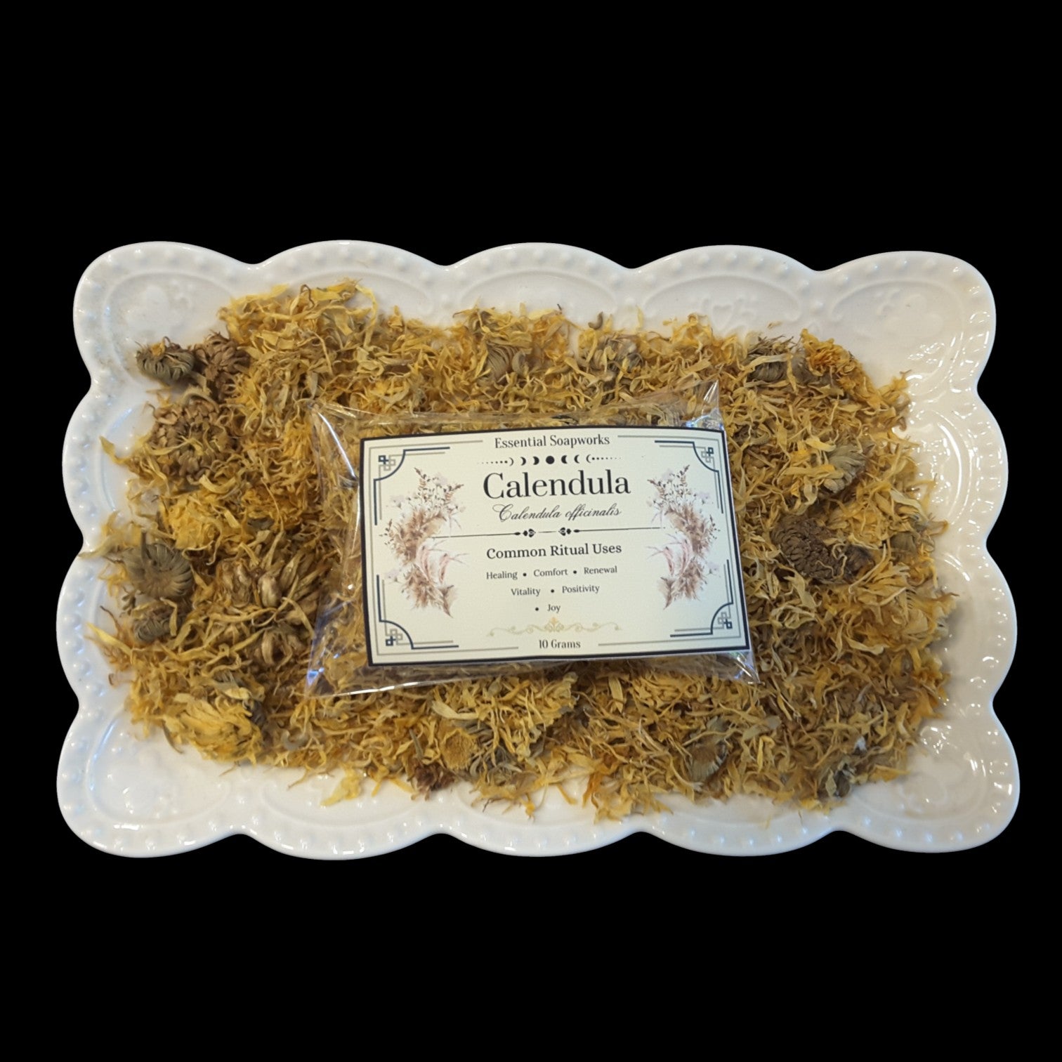A packaged bar of Calendula flowers placed on top of dried calendula flowers arranged on a white scalloped platter, set against a solid black background.