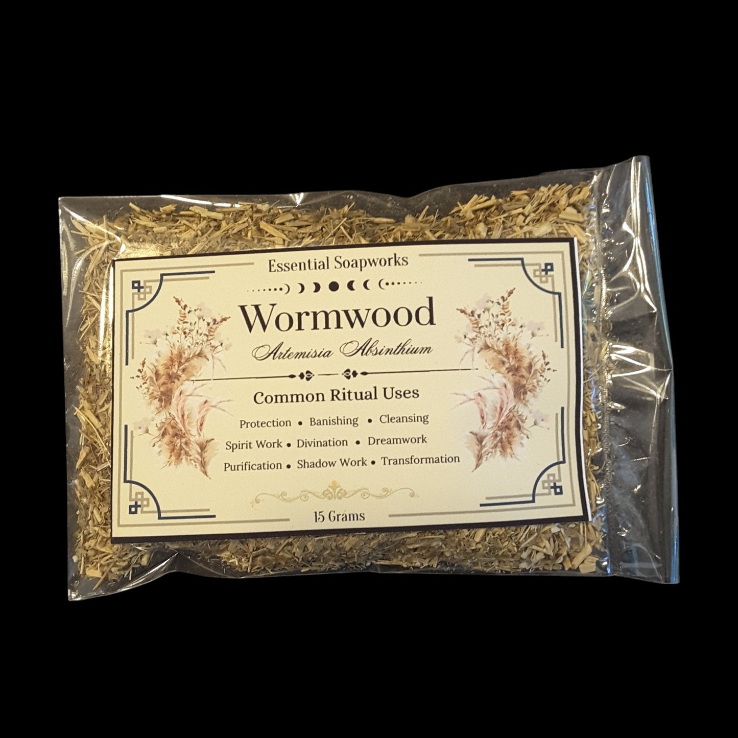 A clear plastic bag containing dried Wormwood herb, with a cream-colored paper label detailing its common ritual uses, set against a solid black background.