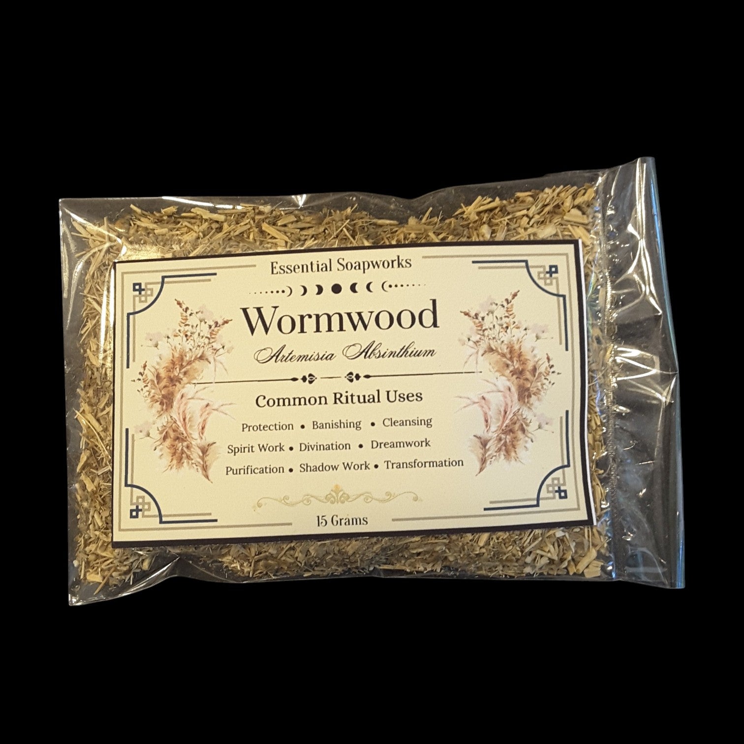 A clear plastic bag containing dried Wormwood herb, with a cream-colored paper label detailing its common ritual uses, set against a solid black background.