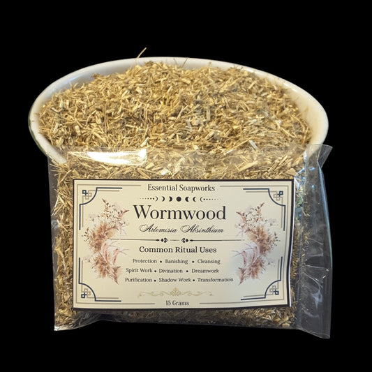 A clear plastic bag filled with dried wormwood herb, with a white bowl of the same herb on top and a front label reading 'Essential Soapworks Wormwood' on a black background.