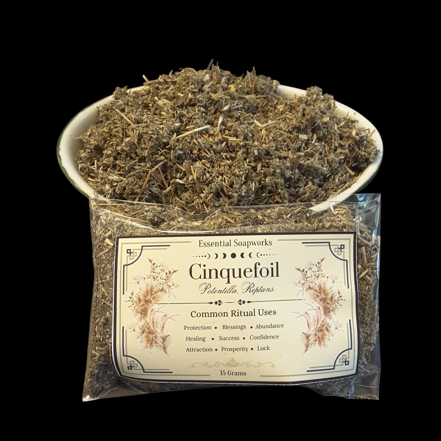 A clear plastic bag of Essential Soapworks 'Cinquefoil'  with a white ceramic bowl filled with the same dried herbs, set against a solid black background.
