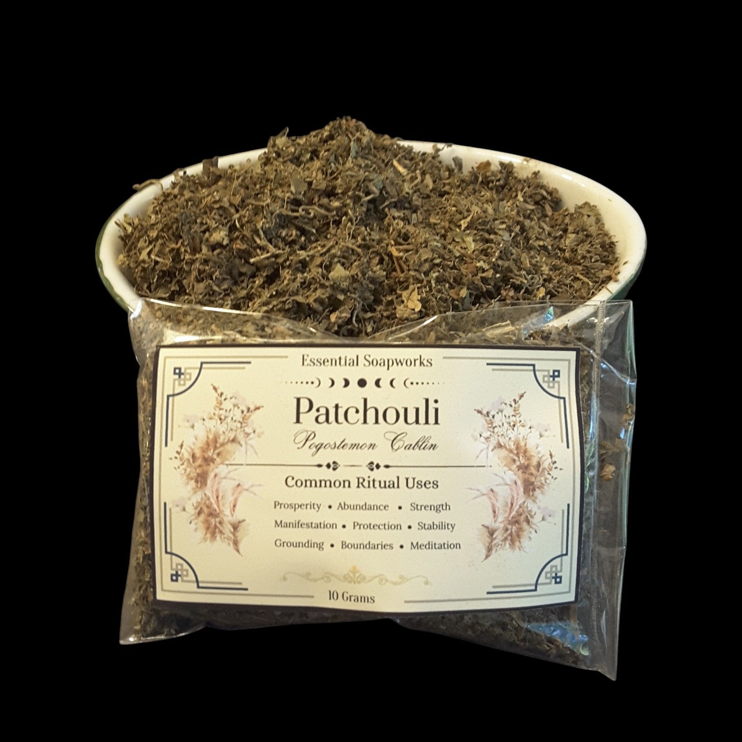 Patchouli herb, shown as a white bowl filled with dried green-brown patchouli leaves above a clear plastic bag containing 10 grams of the same blend, set against a solid black background.
