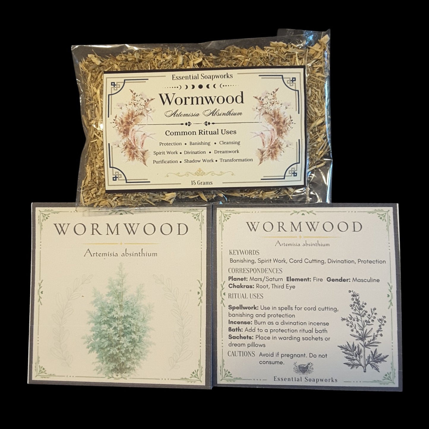 Three wormwood essential soapworks products arranged on a black background: a clear plastic bag of loose dried wormwood leaves at the top, and two square printed cards below with wormwood labels and botanical illustrations.