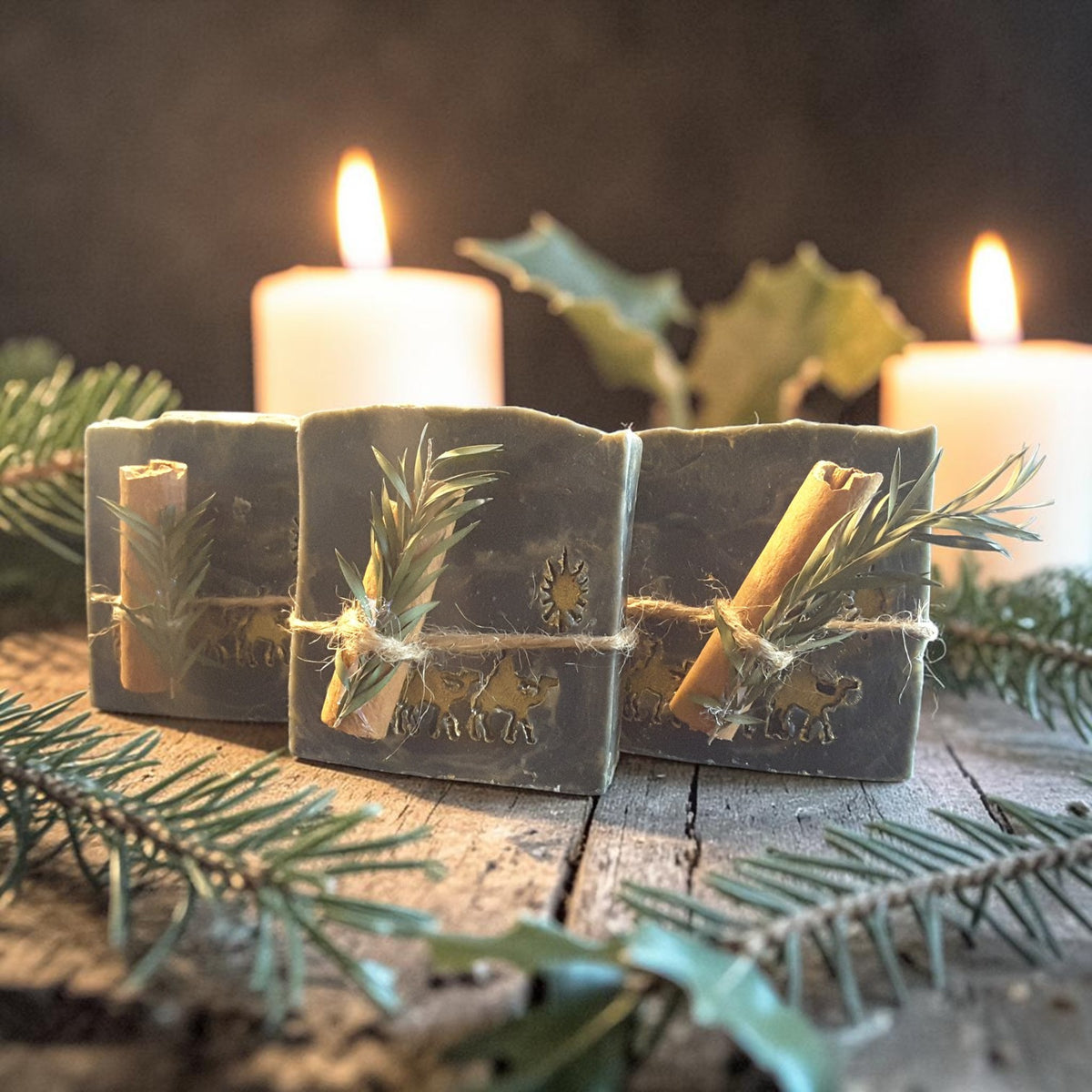 winter solstice soap tied with twine and a cinnamon stick along with greenery on a wooden surface with pine needles and candles in the background
