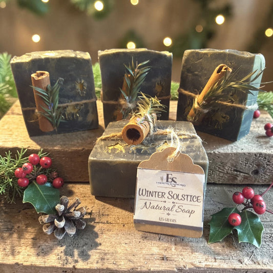 winter solstice soap tied with twine and a cinnamon stick along with greenery on a wooden surface with pine cones and holly
