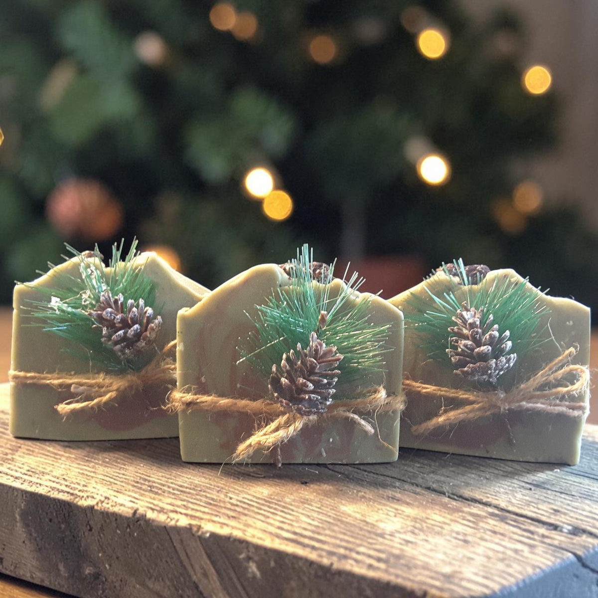 three bars of alpine frost christmas soap on a wooden surface with a christmas tree in the background