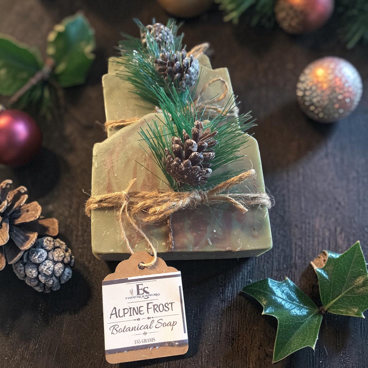 three bars of alpine frost christmas soap on a wooden surface with pine cones