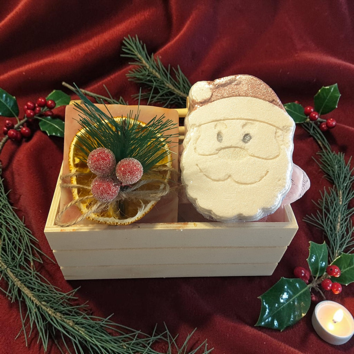 cranberry orange spa gift set featuring cranberry orange soap, santa shaped bath bomb, bamboo soap ladder and loofah in a wooden crate on a red fabric surface