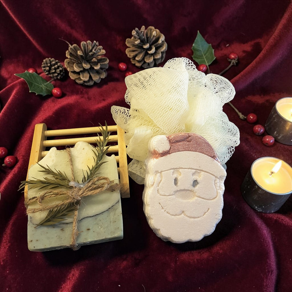 eucalyptus mint christmas gift crate spa kit featuring eucalyptus mint soap, santa shaped bath bomb, bamboo soap ladder and loofah on a red fabric surface with tealight candles and pine cones